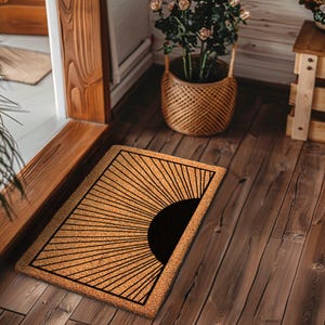 May include: A brown coir doormat with a black sunburst design. The sunburst design is made up of thin lines radiating out from a black circle in the center of the mat.