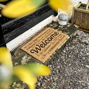 May include: A brown coir welcome mat with the word "Welcome" in large black lettering. The mat also features the word "Welcome" in multiple languages, including "Bem-vindo", "Hi Wilkin", "Salut", "Khush Amdeed", "Velkommen", "Be", "Witamy", "Willkommen", "B", "Vilejte".
