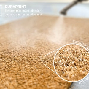 Op de afbeelding: Close-up van een bruine deurmat met een witte cirkel die de textuur van de vezels accentueert. De tekst "EXCLUSIVE DURAPRINT TECHNOLOGY" staat in een witte cirkel rond de close-up.