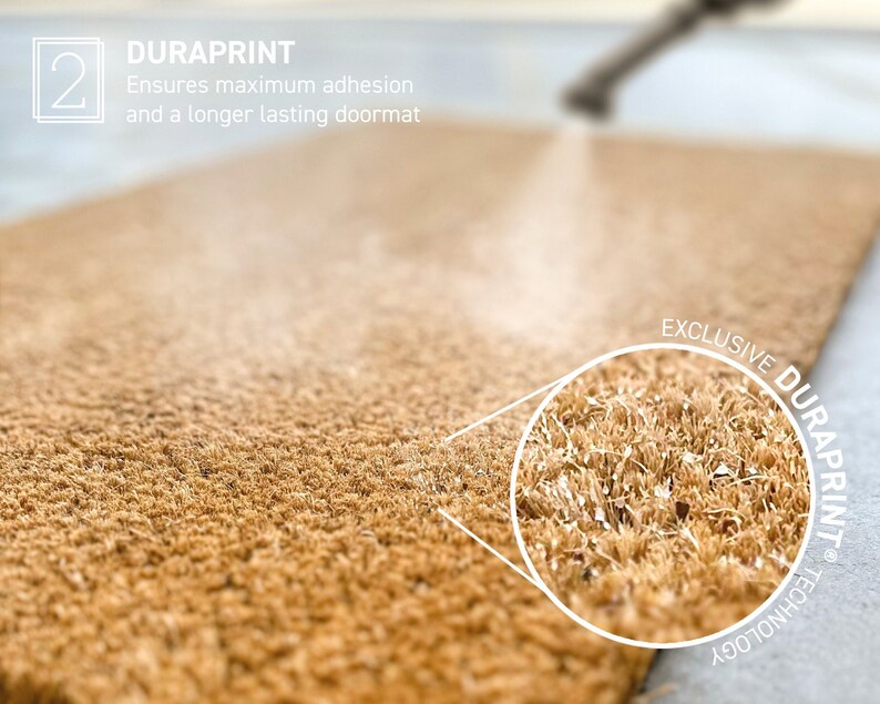 Op de afbeelding: Close-up van een bruine deurmat met een witte cirkel die de textuur van de vezels accentueert. De tekst "EXCLUSIVE DURAPRINT TECHNOLOGY" staat in een witte cirkel rond de close-up.