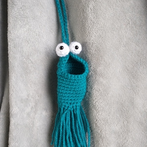 Könnte beinhalten: Hängender tealblauer Häkel-Anhänger mit weißen Glitz Augen und einem Fransen-Saum.