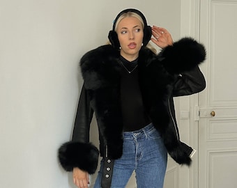 May include: A black leather jacket with a fur collar and cuffs. The jacket has a belt and is worn with blue jeans and black boots.