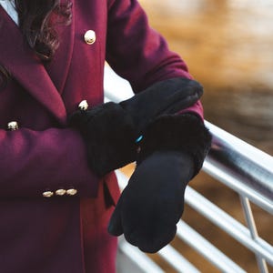 Può includere: Un cappotto doppiopetto bordeaux con bottoni dorati e guanti neri con finiture in ecopelliccia. Il cappotto ha un design classico e i guanti sembrano caldi ed eleganti.