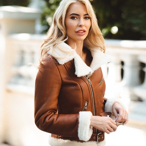May include: A brown leather jacket with a white shearling collar and lining. The jacket has a zipper closure and a belt at the waist.