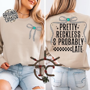 May include: A tan sweatshirt with a black and white checkered bow on the front and the text "Pretty Reckless & Probably Late" with a black and white checkered ribbon and a turquoise heart on the back.