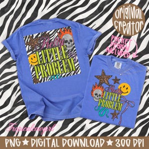 May include: A blue t-shirt featuring a graphic design with the text Pretty LITTLE PROBLEM, a skull with flames, a yellow smiley face, a leopard print star, and a purple ribbon. The design is displayed on both the back and the front pocket area.