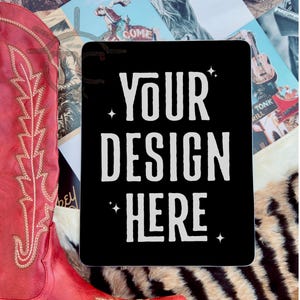 May include: A black square sticker with white text that reads "YOUR DESIGN HERE" with small white stars on either side of the text. The sticker is on a brown and black striped surface.