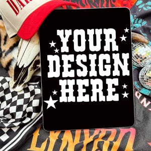May include: A black laptop with a white design that says "YOUR DESIGN HERE" with stars on either side. The laptop is surrounded by various colorful items, including a red and white baseball cap, a black and white checkered bandana, and a tiger print fur.