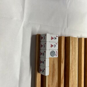 May include: A set of white dominoes with red numbers and symbols on a wooden rack. The dominoes are numbered 1 through 9 and include a joker.