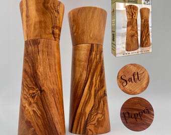 May include: Two tall, tapered salt and pepper mills crafted from olive wood with distinct natural grain patterns. The set includes a box labeled HANDMADE OLIVE WOOD SALT & PEPPER MILL GRINDERS and two circular wooden discs marked Salt and Pepper.