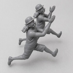 May include: Two gray figurines of clowns in mid-air, with arms raised and legs extended as if running. Each clown wears a hat, shorts, and a tank top. They have large red noses and exaggerated facial features.