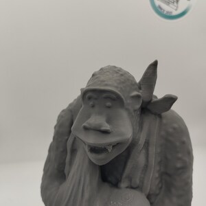 May include: A gray 3D printed figurine of a monkey wearing a bandana and holding a round object. The monkey has a wide mouth and large teeth.