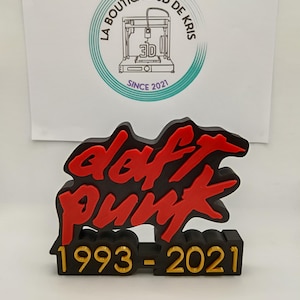 Puede incluir: Un logotipo de Daft Punk impreso en 3D en negro y rojo con el texto "1993-2021" en dorado. El logotipo está sobre una base negra.