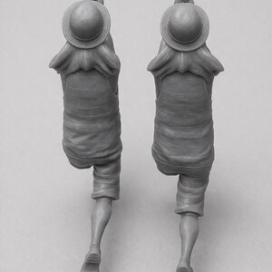 May include: Two gray figurines of a person in a straw hat, shirt, and shorts, with hands clasped in prayer. The figures are in a walking pose, with one leg bent. The hat has a round top and a wide brim.