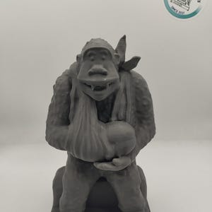 May include: A gray 3D printed figurine of a monkey holding a bag. The monkey is wearing a bandana and has a mischievous expression.