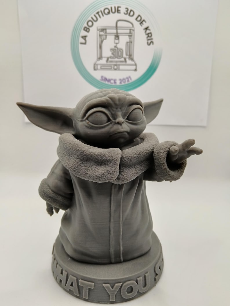 Puede incluir: Una figura impresa en 3D de color gris de un personaje de la franquicia Star Wars, conocido como "The Child" o "Baby Yoda". La figura est&aacute; de pie sobre una base con el texto "What You Say" impreso en ella.