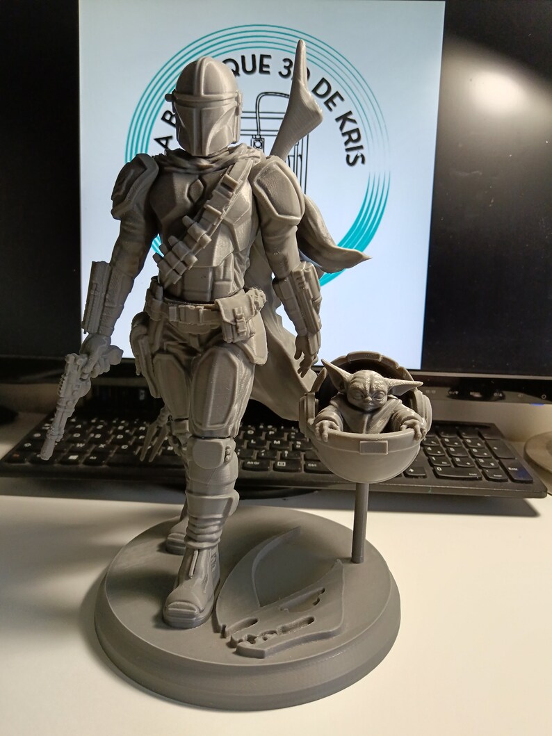 May include: A gray 3D printed figurine of a Mandalorian character from Star Wars, holding a small gray 3D printed figurine of the character Grogu, also known as Baby Yoda, in a floating pod.