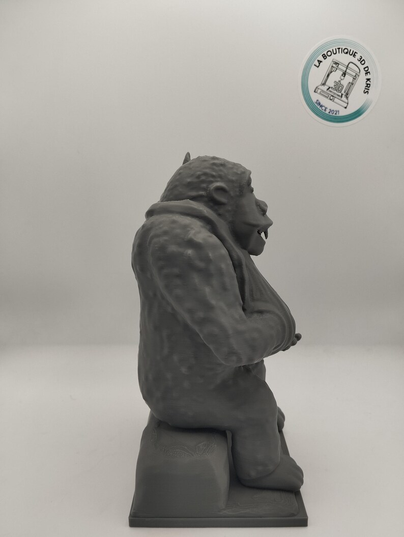 May include: A gray 3D printed figurine of a gorilla sitting on a small platform. The gorilla is in a seated position with its arms crossed and its head tilted slightly to the side.
