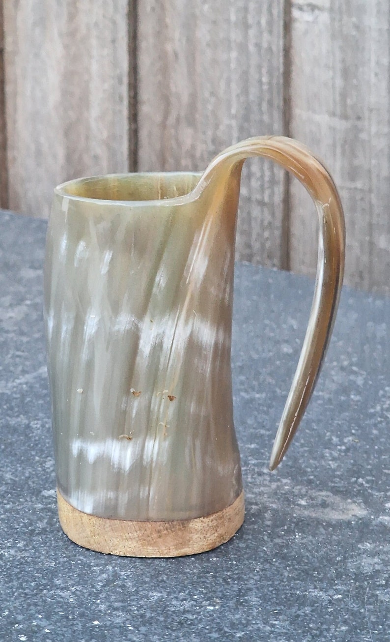 Peut inclure: Une tasse &agrave; boire en corne brune et blanche avec une base en bois. La tasse a un motif naturel unique et une poign&eacute;e incurv&eacute;e.