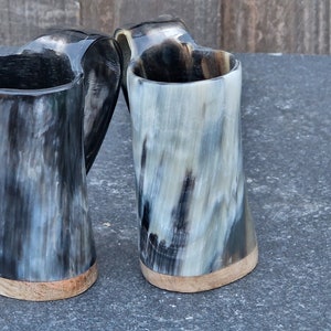 Peut inclure: Deux mugs en corne noire et blanche avec des bases en bois. Les mugs sont faits de corne naturelle et ont un aspect rustique unique.