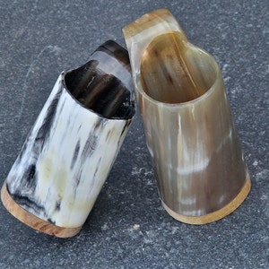 Peut inclure: Deux tasses &agrave; boire en corne polie avec une base en bois. Les tasses sont de couleur brun clair avec des stries brun fonc&eacute;.