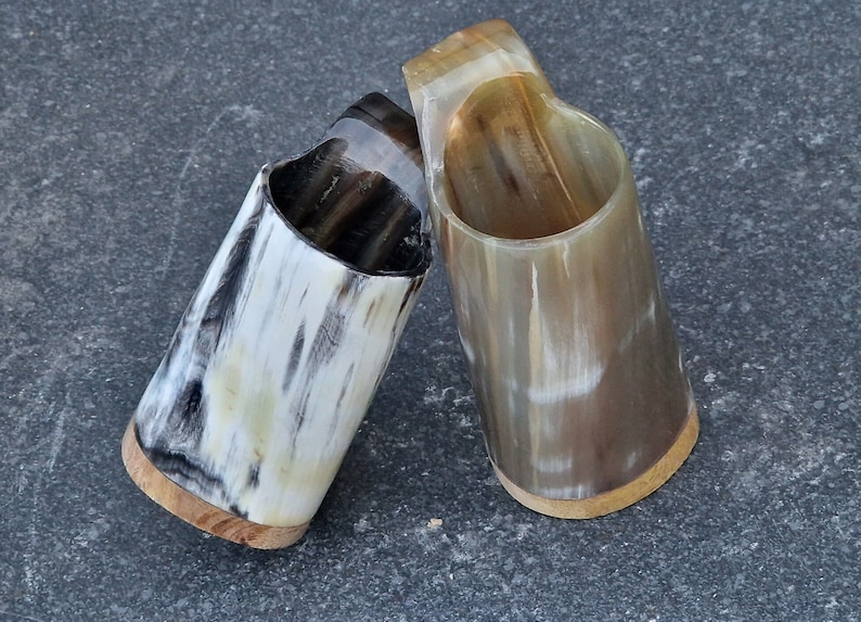 Peut inclure: Deux tasses &agrave; boire en corne polie avec une base en bois. Les tasses sont de couleur brun clair avec des stries brun fonc&eacute;.