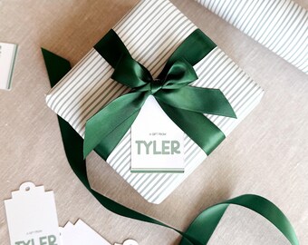 May include: A wrapped gift with a green satin bow and matching ribbon. The gift is wrapped in striped paper and has a tag that reads "A Gift From Tyler". Several gift tags with the same text are scattered around the gift.