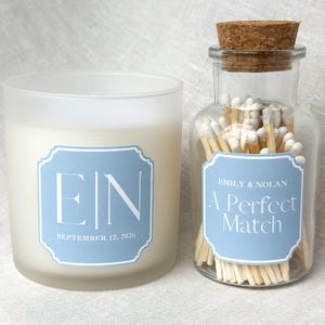 May include: A frosted glass candle and a glass jar filled with matches. Both have light blue labels with white text. The candle label reads "EIN" and "September 12, 2026." The jar label says "Emily & Nolan" and "A Perfect Match."