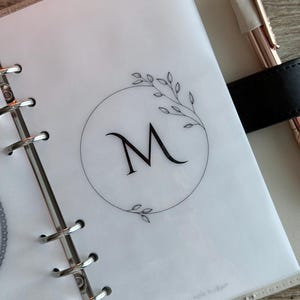 May include: A white ceramic mug with a black handle and the text "But First, Coffee" in a bold, black font. The mug is filled with a dark liquid, likely coffee, and sits on a light-colored surface.