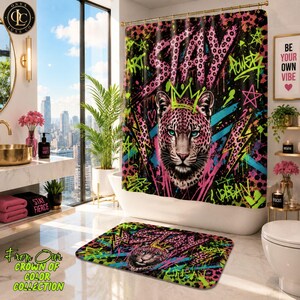 May include: A shower curtain and matching bath mat featuring a vibrant graffiti-style design with a central leopard head wearing a crown. The black background is accented with neon pink, blue, and green patterns, stars, and the text STAY and ART.