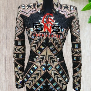 May include: Black show shirt with a geometric pattern of beige and iridescent rhinestones. The shirt has a zipper closure and a collar. The text "SNS SHOW SHIRT" is on the front of the shirt.