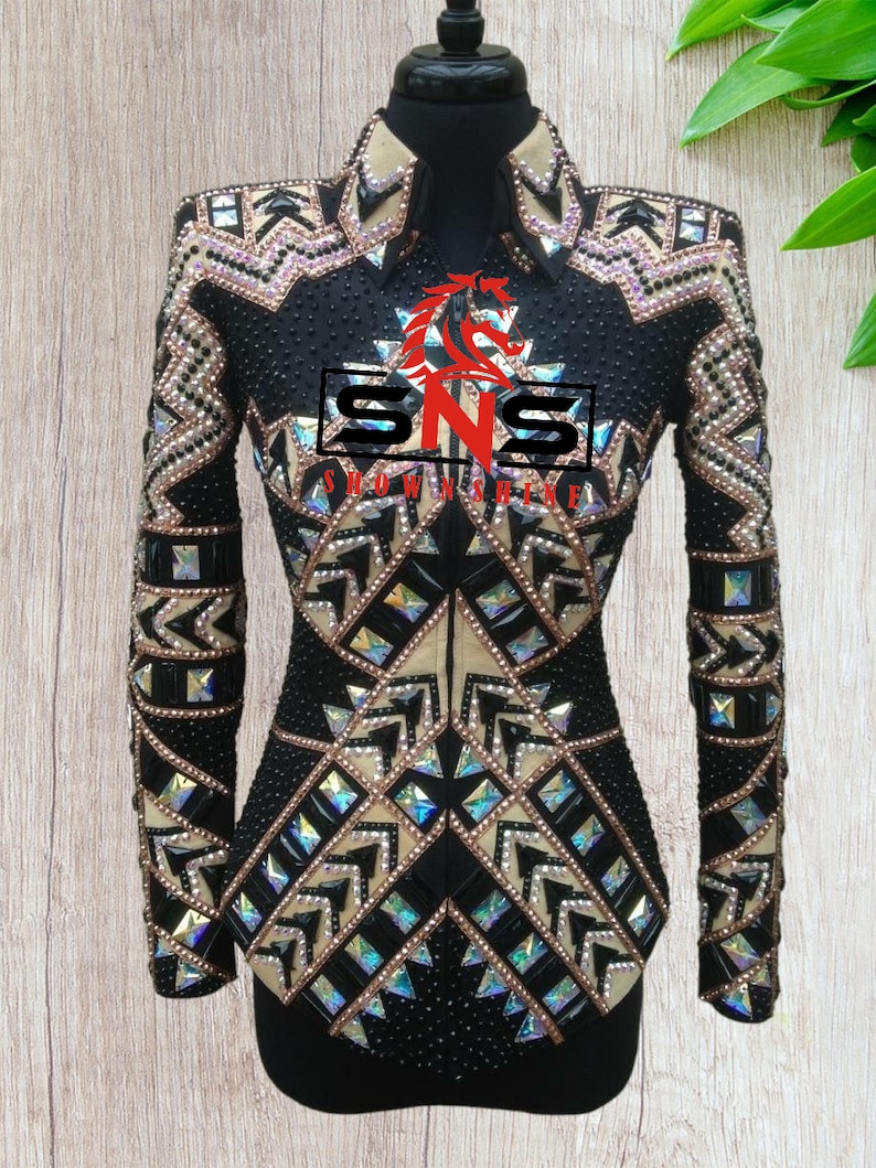 May include: Black show shirt with a geometric pattern of beige and iridescent rhinestones. The shirt has a zipper closure and a collar. The text "SNS SHOW SHIRT" is on the front of the shirt.