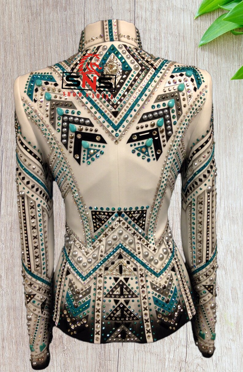 K&ouml;nnte beinhalten: Wei&szlig;e Showjacke mit geometrischem Design mit t&uuml;rkisfarbenen, schwarzen und silbernen Verzierungen. Die Jacke hat einen Stehkragen und lange &Auml;rmel.