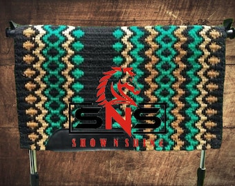 May include: A black, tan, and teal saddle pad with a diamond pattern. The saddle pad has a black leather trim and the text "SHOWNSHE" is visible on the bottom.