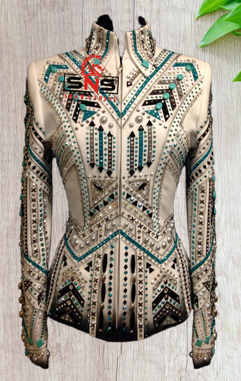 K&ouml;nnte beinhalten: Wei&szlig;e Showjacke mit geometrischem Design mit t&uuml;rkisfarbenen, schwarzen und silbernen Verzierungen. Die Jacke hat einen Rei&szlig;verschluss und lange &Auml;rmel.