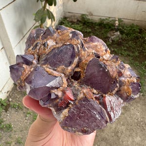 May include: A cluster of deep purple amethyst crystals featuring sharp, pointed terminations and translucent facets. The crystal formation is interspersed with veins of brownish-orange mineral deposits, creating a textured, multi-faceted appearance.