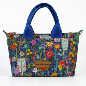 May include: A tote bag with blue fabric handles and a zipper closure, featuring a colorful pattern of stylized cats and flowers on a dark blue background. A rectangular brown label with the text Such-n-Sew Studio is centered on the front.