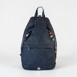 May include: A dark navy blue sling backpack with a teardrop shape, featuring a top handle and a front zippered pocket. The upper section displays a dark blue fabric panel with a colorful pattern of jellyfish and various sea creatures.
