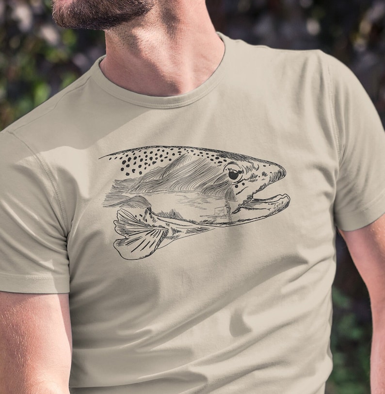 May include: A beige t-shirt featuring a black and white line drawing of a trout fish on the front.