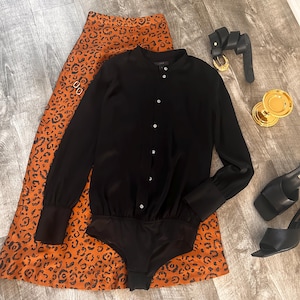 May include: A black long-sleeved button-up shirt with a mock neck and a leopard print skirt.