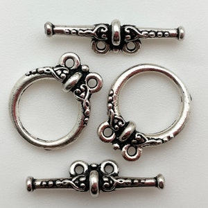 May include: Three silver-toned toggle clasps with ornate designs. Each clasp features a decorative ring and a bar with a loop on each end.