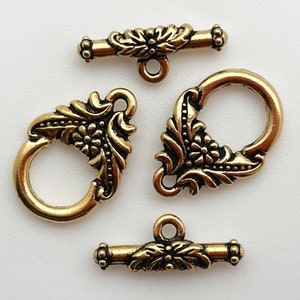 May include: Three gold-tone metal clasps with ornate floral designs. The clasps are designed for jewelry making and feature a toggle closure.