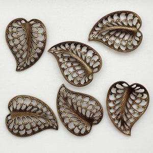 May include: Six ornate metal leaf charms in a bronze finish. Each charm features a delicate filigree design with a heart-shaped outline.