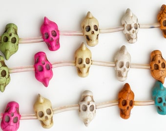 May include: A string of colorful skull beads, featuring various shades of green, pink, white, and brown. The beads are strung on a clear elastic cord and are perfect for making jewelry or adding a unique touch to any craft project.