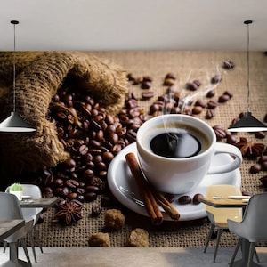 May include: A white coffee mug filled with steaming coffee sits on a white saucer with a cinnamon stick. The mug is surrounded by coffee beans and a burlap sack.