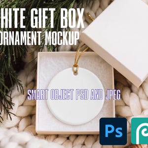 May include: A white circular ceramic ornament with a gold hanging string, presented inside an open square white gift box. The text WHITE GIFT BOX ORNAMENT MOCKUP and SMART OBJECT PSD AND JPEG is visible, along with Photoshop and Photopea icons.