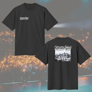 May include: A black short-sleeve t-shirt featuring the text Kansas City in a stylized white font on the upper left chest. The back of the shirt displays a black and white graphic of the Kansas City skyline with the text Kansas City above it.