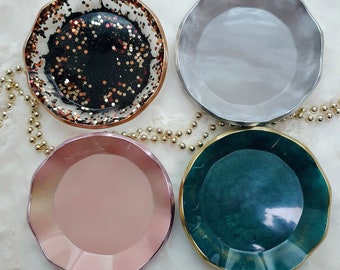 May include: Four decorative resin coasters with a wavy edge. The coasters are in four different colors: black with gold glitter, light pink, light gray, and dark green.