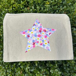 Puede incluir: Una bolsa de lona beige con cremallera con un diseño de estrella de estampado floral rosa, blanco y azul.