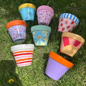 以下が含まれることがあります： さまざまなデザインが描かれたテラコッタ製の植木鉢が8個あります。鉢はピンク、ブルー、イエロー、オレンジ、ホワイトなど、さまざまな色で、ストライプ、花、水玉模様などがあります。